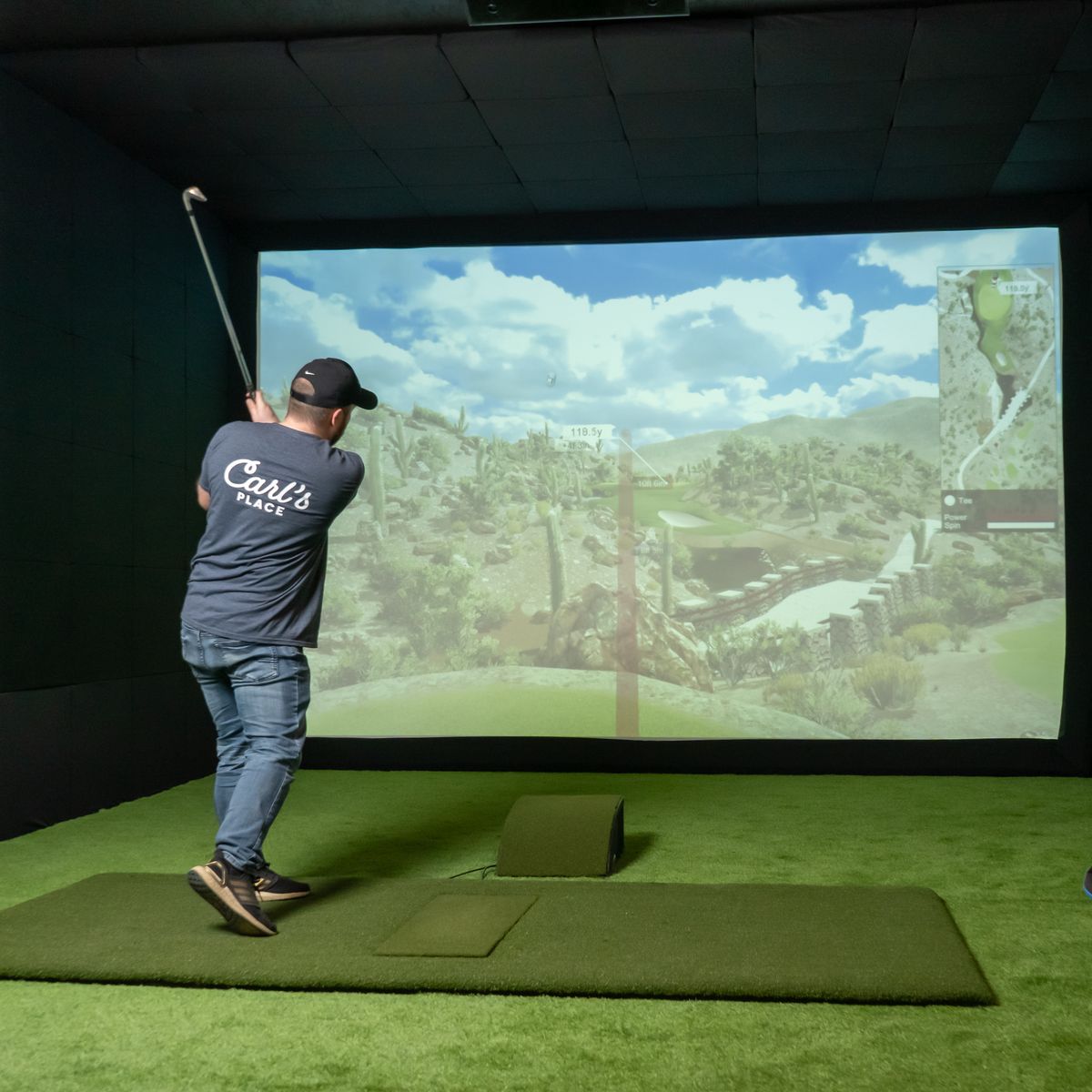 Golfer in golf simulator with enclosure to protect projector on floor